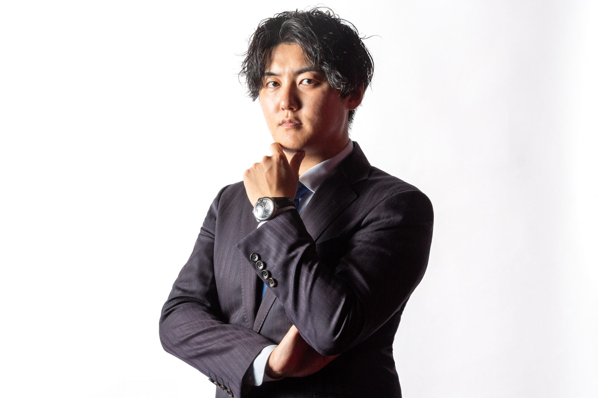 スーツ姿で腕を組み、真剣な眼差しで前を見据える男性のポートレート写真