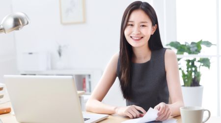 デスクでパソコンを使いながら微笑むビジネス女性のイメージ写真