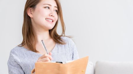 ノートにメモを取りながら前向きに微笑む女性のイメージ写真