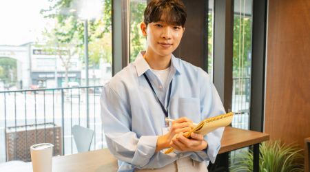 明るいカフェでノートを開き微笑む若い男性のイメージ写真