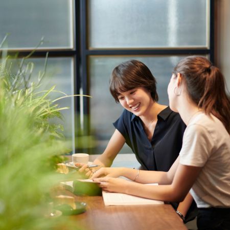 カフェのような落ち着いた空間で、女性同士が笑顔で相談している様子の写真