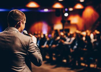 多くの聴衆の前でスピーカーが講演する様子。学びと刺激を得るイベントを象徴するイメージ。