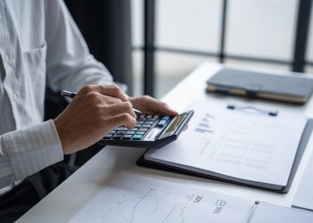 ビジネス資料と電卓を用いながら分析作業を行う手元の写真。現状把握と課題分析を象徴するイメージ。